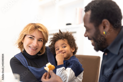 small child  half African and half Caucasian  in his mother s arms  looking at his father with a playful expression  moments of joyful life of a mixed race family