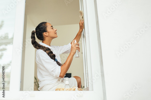 Young woman washing window using spray and natural rag.
