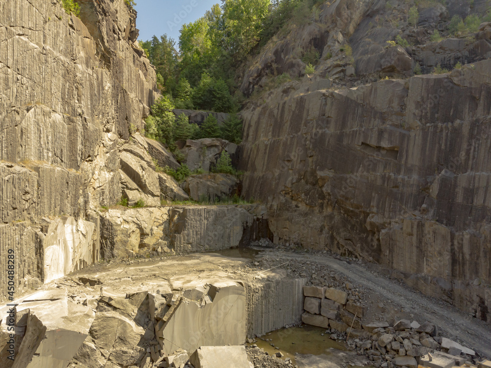 Under a blue sky is a view of a deep rock quarry where granite rocks