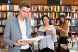 Young positive male student browsing textbooks in university library