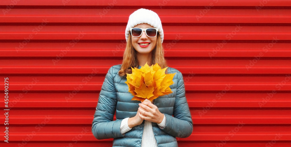 Fototapeta premium Autumn portrait of happy smiling young woman holding an yellow maple leaves on a red background