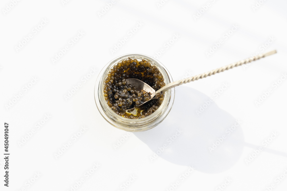 Caviar black in glass jar on a silver spoon, selective focus Caviar black in glass jar on a silver spoon, selective focus