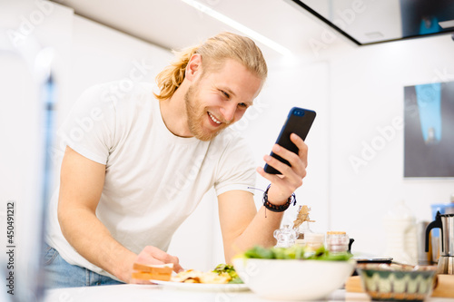 Young white man using cellphone while having lunch in kitchen