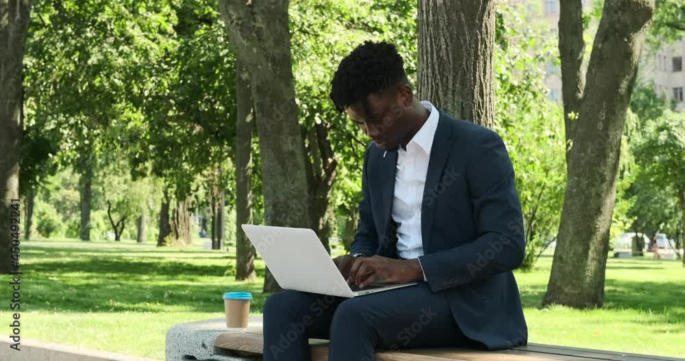 African american businessman working on laptop outdoors at city park