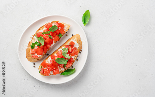 Two sandwiches with tomato, cheese, basil on a fried baguette on a gray background.