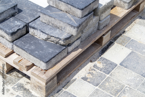 Concrete or paved gray paving slabs or floor or walkway stones stacked on a pallet. Concrete paving slabs in the backyard or road paving. Garden brick path in the courtyard on a sandy foundation.