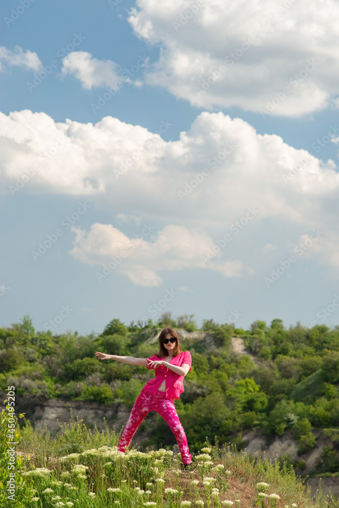young girl in pink posing in green grass in a field, against a background of a cloudy sky