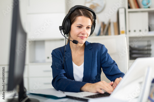 фотографія Portrait of positive woman call center operator receiving calls and using laptop