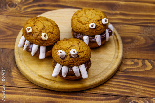 Halloween dessert: Toothed monsters made of oatmeal cookies, chocolate spread and marshmallows on a wooden table
