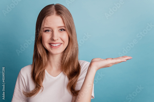 Portrait of charming adorable teen promoter girl hand hold empty space on blue background