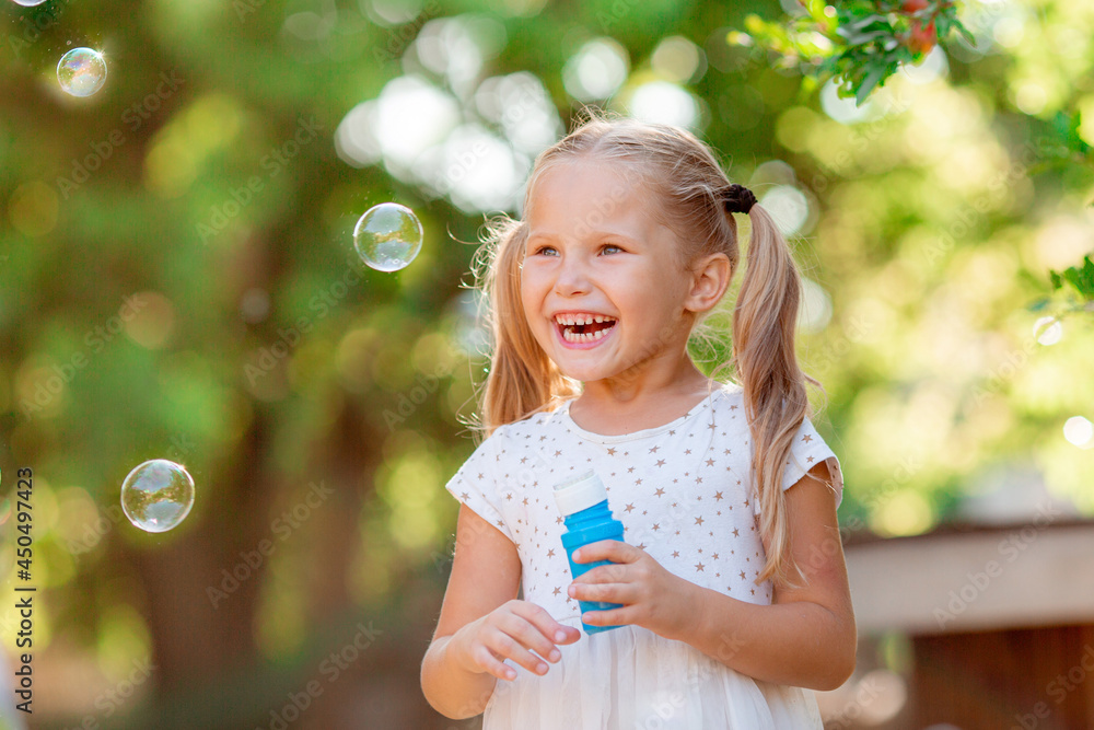 funny little blonde girl blowing soap bubbles in summer in the park funny little blonde girl blowing soap bubbles in summer in the park