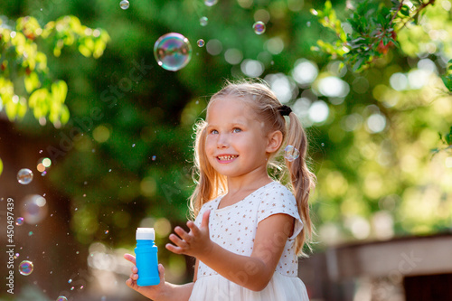 funny funny little blonde girl blowing soap bubbles in summer in the park
