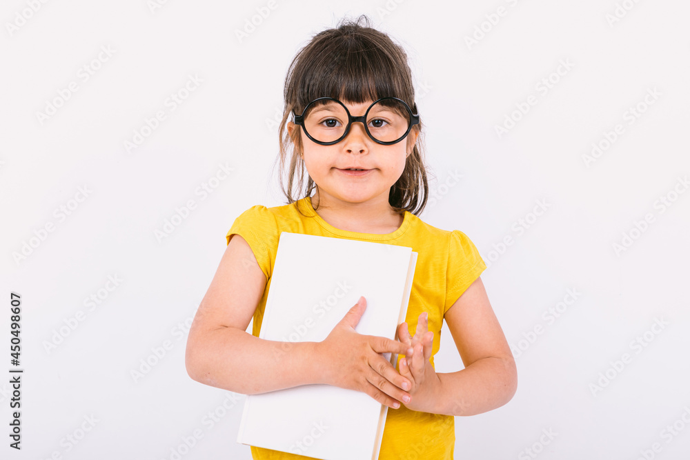Smiling little girl wearing yellow t-shirt and round black glasses holding a book in her hands on white background Smiling little girl wearing yellow t-shirt and round black glasses holding a book in her hands on white background