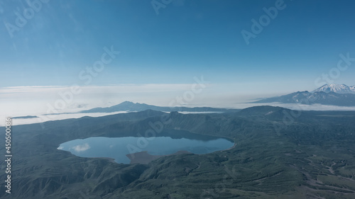 View from the height of Kamchatka. Among the mountains, you can see a picturesque lake with a mirror-smooth surface. Reflection of the blue sky and clouds in the water.