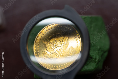 A gold coin lying on a green stone, on a brown background, visible through a magnifying glass. Old coin viewed through a magnifying glass. 