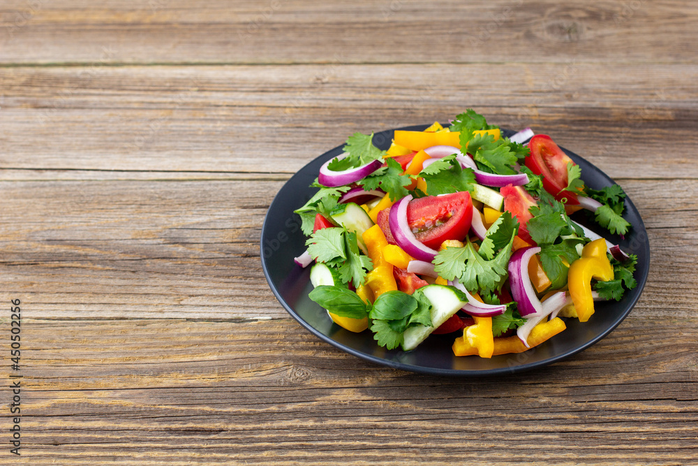 Plate of rainbow salad with different vegetables and herbs on black plate on wooden background