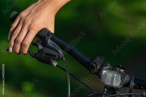 Woman's hand pressing the brakes of a mountain bike in the bright sunlight of a summer day close-up with copy space