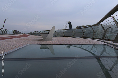 Glass floor of the bridge. Rainy morning view of empty New Pedestrian Bridge against overcast sky. Beautiful autumn colored trees in the background. Stunning Abstract Image photo