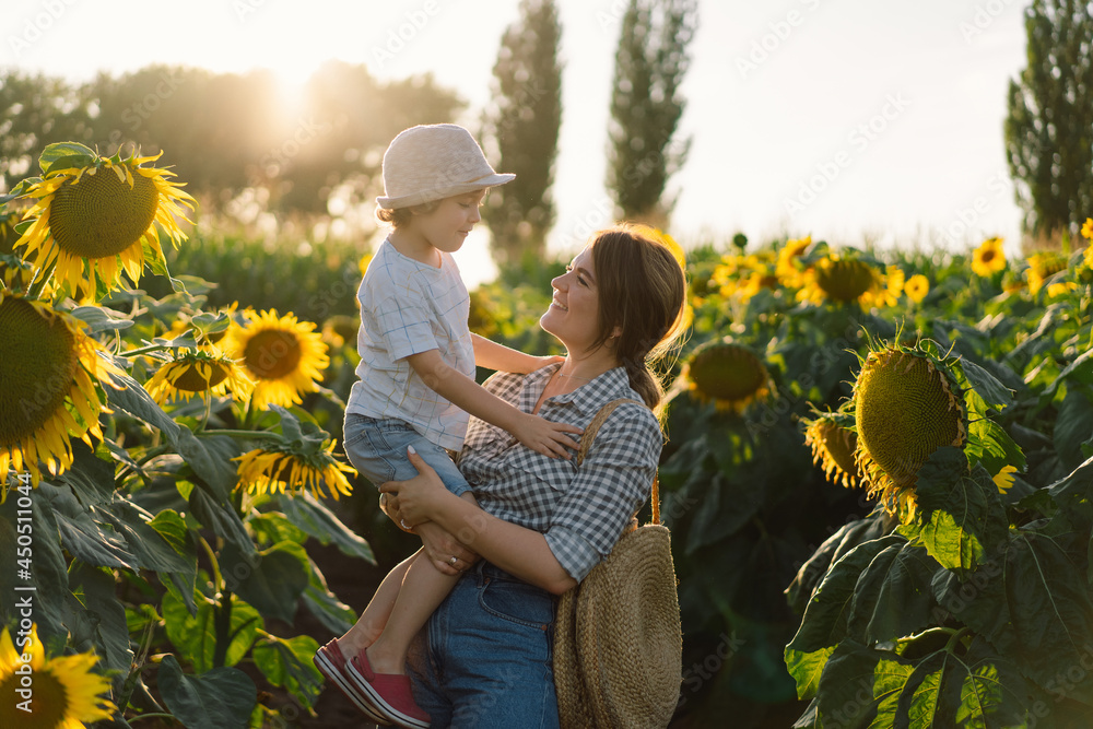 Mother with little baby son in sunflowers field during golden hour. Mom and son are active in nature