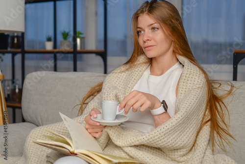 beautiful young woman reads a book at home and drinks coffee in a cozy room in the evening. Morning coffee