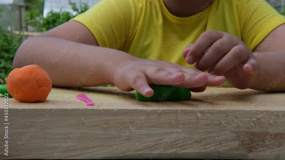 The child sculpts various figures on a wooden board from soft multi-colored plasticine. Close-up The child sculpts various figures on a wooden board from soft multi-colored plasticine. Close-up