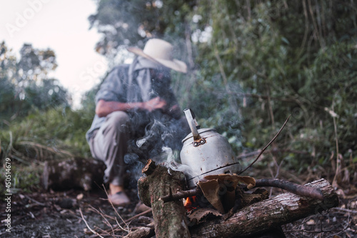 Local farmer making fire to heat water in a rustic kettle .