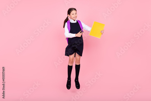 Full body photo of young school girl happy positive smile point finger book notebook ad choice isolated over pink color background