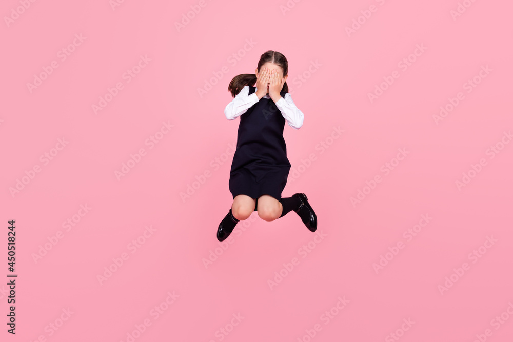 Full length body size photo schoolgirl jumping up covering face with hands isolated pastel pink color background