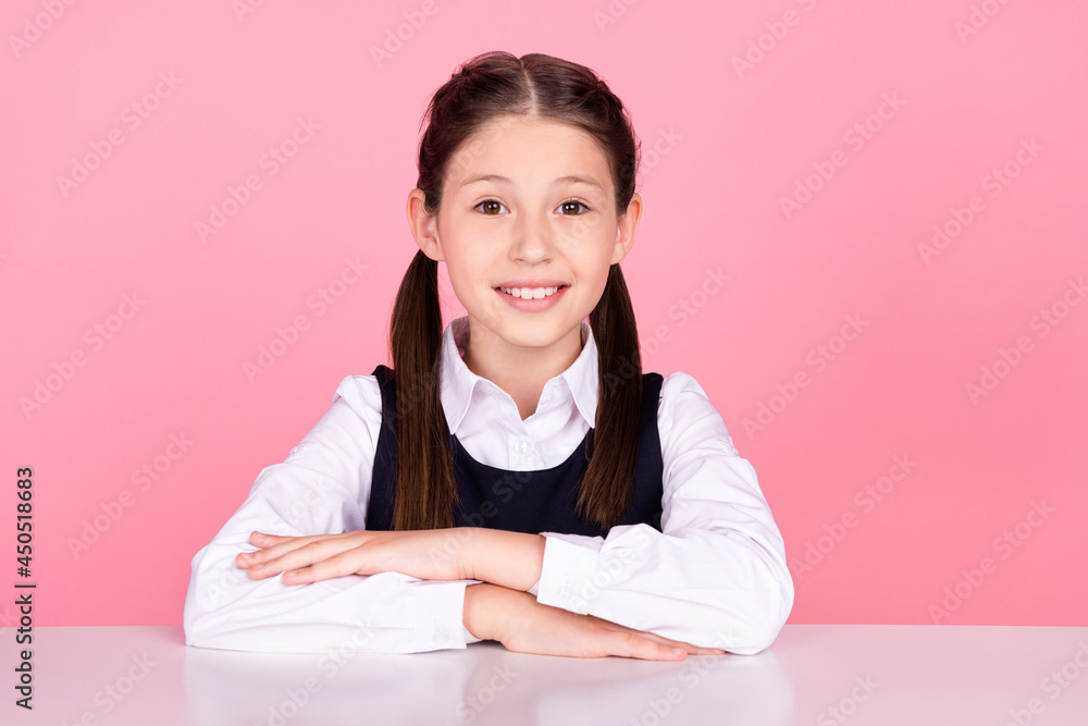 Photo portrait little girl with tails sitting at desk at school smiling isolated pastel pink color background Photo portrait little girl with tails sitting at desk at school smiling isolated pastel pink color background