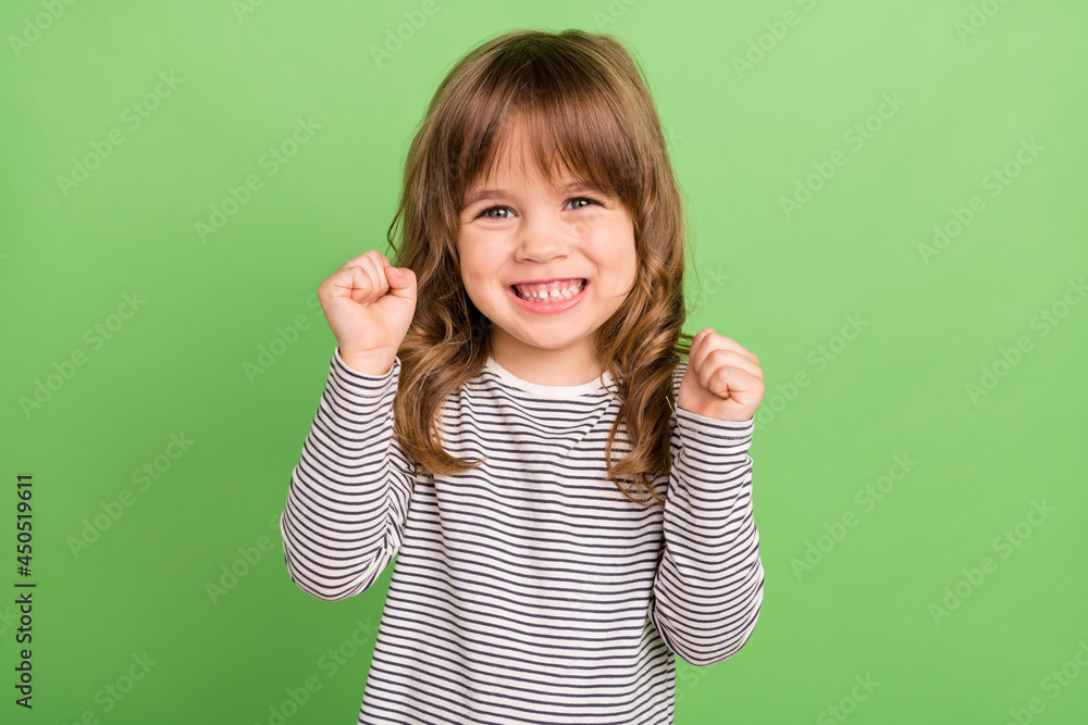 Photo of hooray little blond hair girl hands fists wear striped shirt isolated on green color backgound Photo of hooray little blond hair girl hands fists wear striped shirt isolated on green color backgound