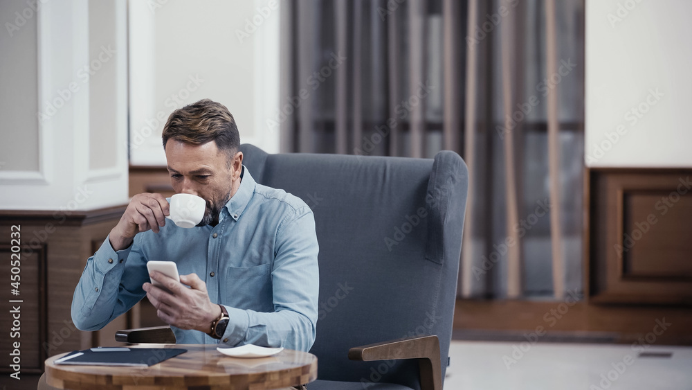 Businessman using smartphone and drinking coffee in lobby of restaurant Businessman using smartphone and drinking coffee in lobby of restaurant