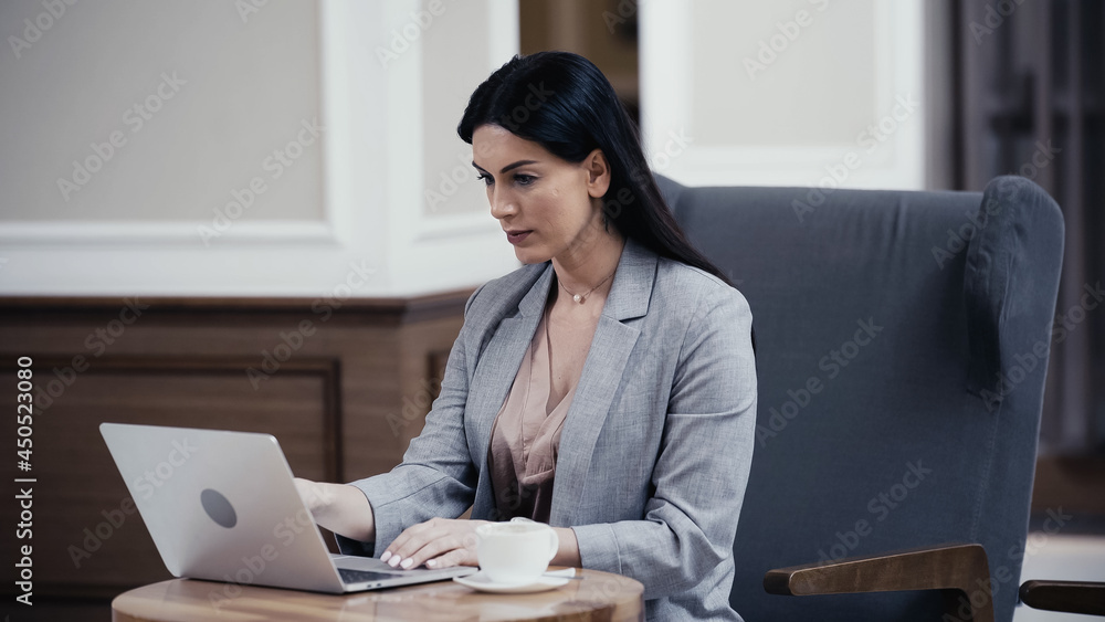 brunette woman looking at laptop near cup of coffee in restaurant brunette woman looking at laptop near cup of coffee in restaurant