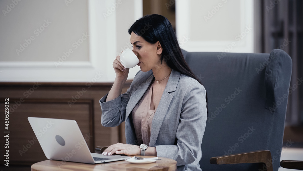 woman drinking coffee while looking at laptop in restaurant woman drinking coffee while looking at laptop in restaurant