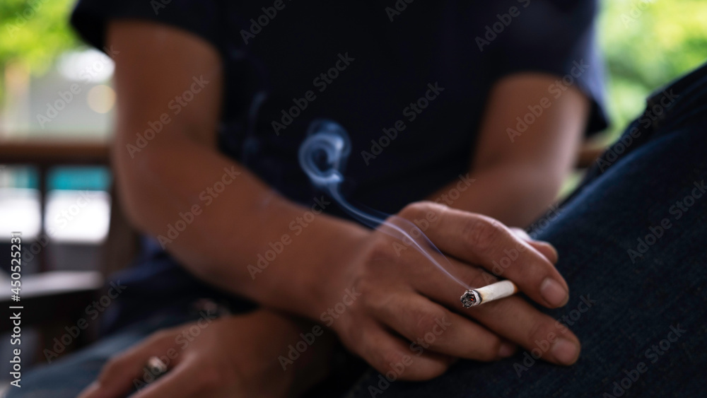 Closeup man cigarette burning smoke in hand. Tobacco smoke spreads carcinogens and the COVID-19 virus to people around. Smoking is health-destroying substance abuse.