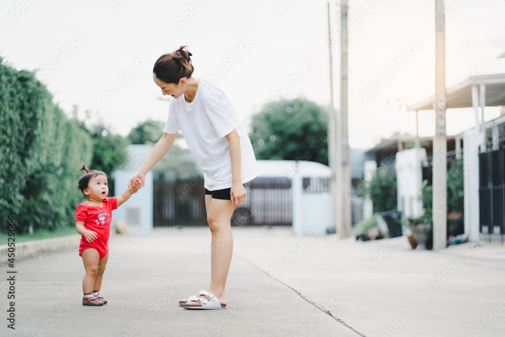 baby step in outdoor to practice balance walk in development according to the age of the child with mother helping daughter support