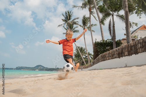 Boy playing barefoot soccer on the beach with a black and white ball on an island by the sea