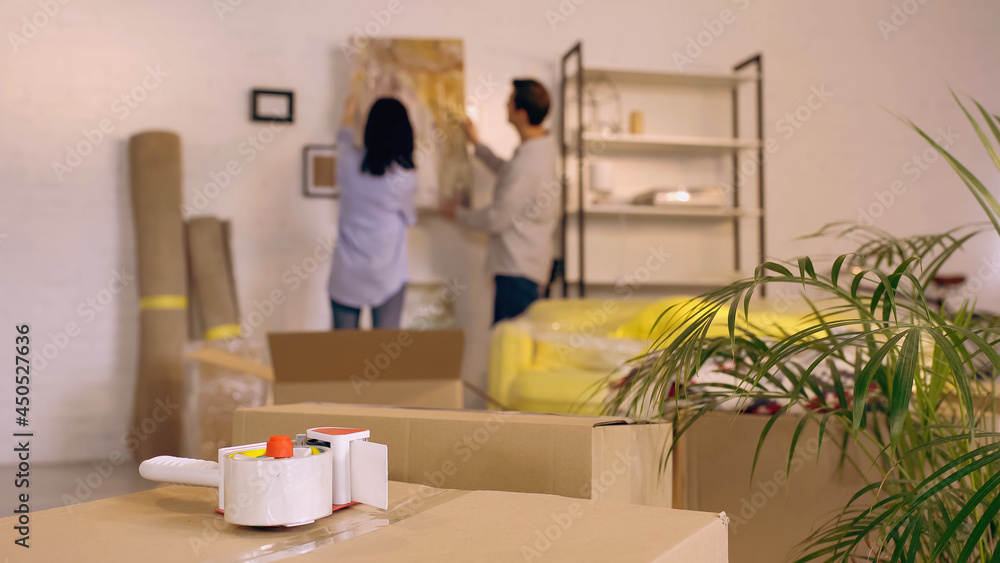 scotch tape on boxes near blurred couple hanging painting in new home scotch tape on boxes near blurred couple hanging painting in new home