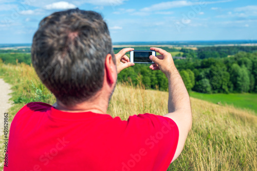 Young male tourist photographs with telephone camera the landscape of the mountain on a camping summer tour.