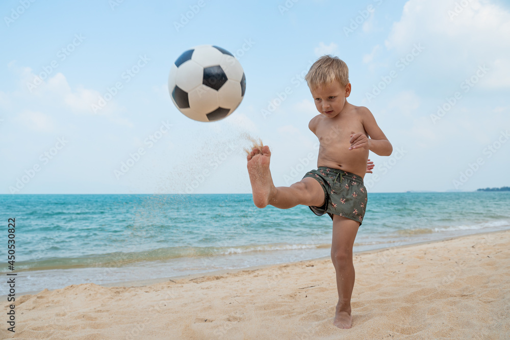 Boy playing barefoot soccer on the beach with a black and white ball on
