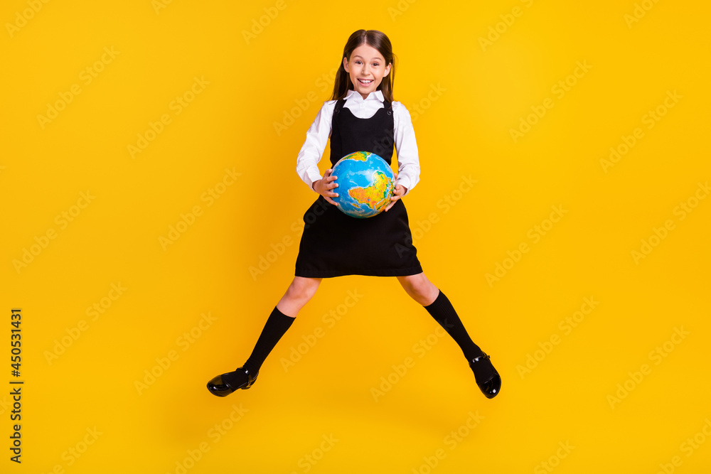Full length body size photo small schoolgirl jumping up keeping globe at school isolated vivid yellow color background