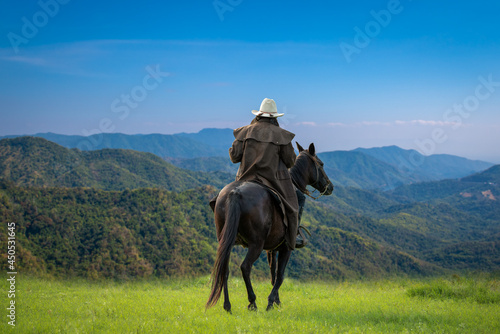 Cowboy horseback riding transportation at sunset time with green mountain and sunlight ray sky background. © APchanel