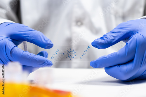 Virus covid-19 sign on glass slide holded by medical personnel with protective gloves