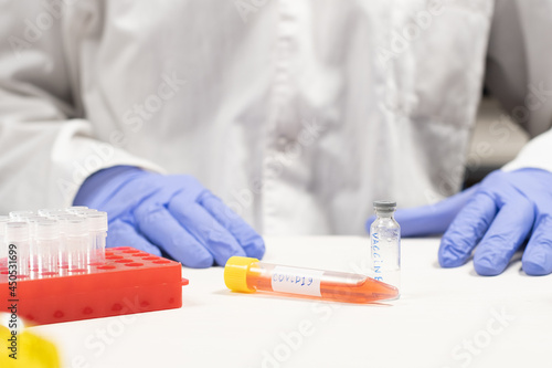 Test tube with covid sign near bottle with vaccine and scientist on the background