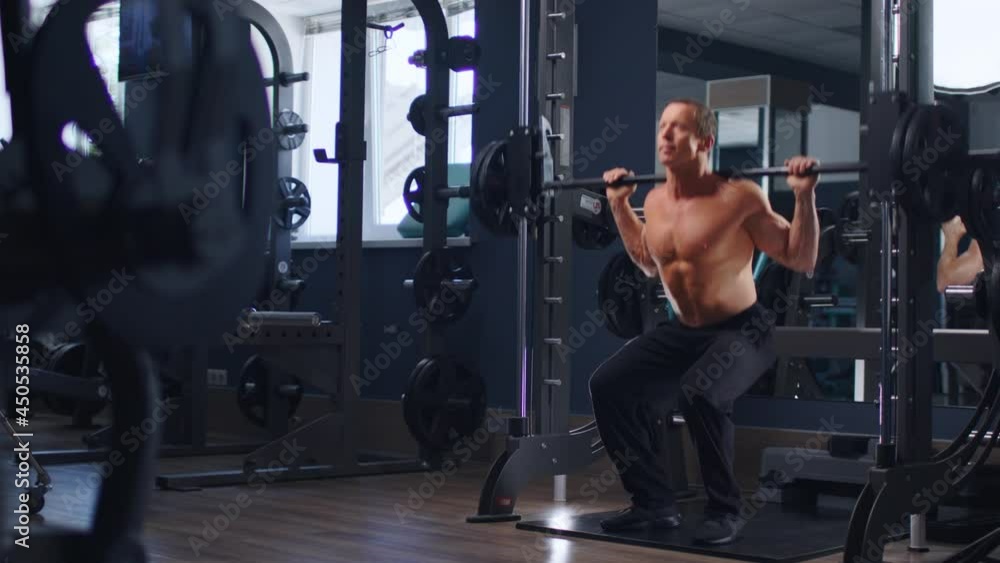 Senior fit man bodybuilder doing barbell squats at gym Senior fit man bodybuilder doing barbell squats at gym