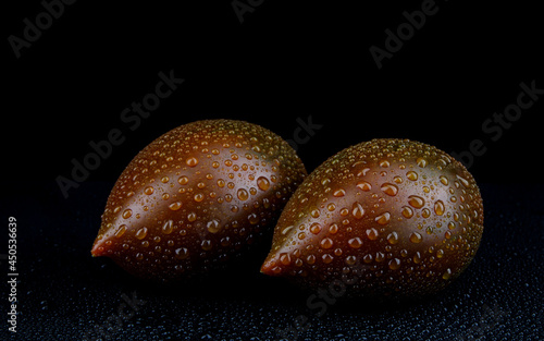 Two ripe cumato tomatoes with drops of water on the peel on a black background.