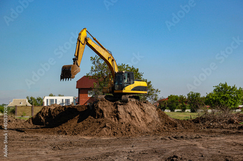 Yellow excavator on a mountain of bright brown earth, construction work