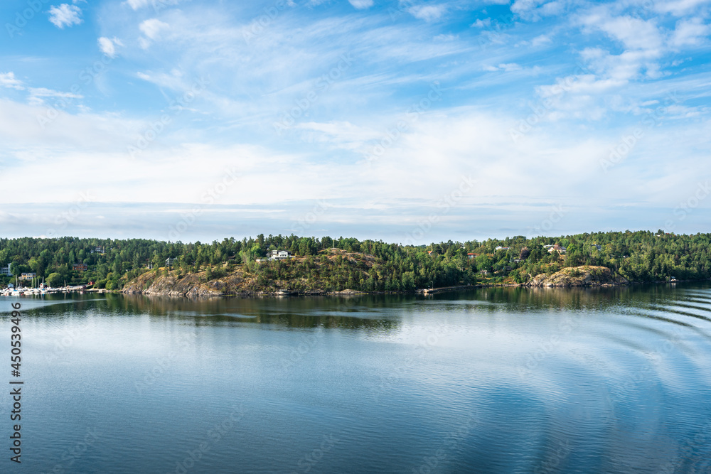 Amazing panoramic view of beautiful evergreens small islands and rocky coast of Scandinavia on sunny summer day. Shot from cruise ship. Forest green long coastline. Water voyage to Sweden Stockholm.