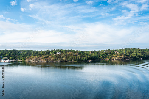 Amazing panoramic view of beautiful evergreens small islands and rocky coast of Scandinavia on sunny summer day. Shot from cruise ship. Forest green long coastline. Water voyage to Sweden Stockholm.