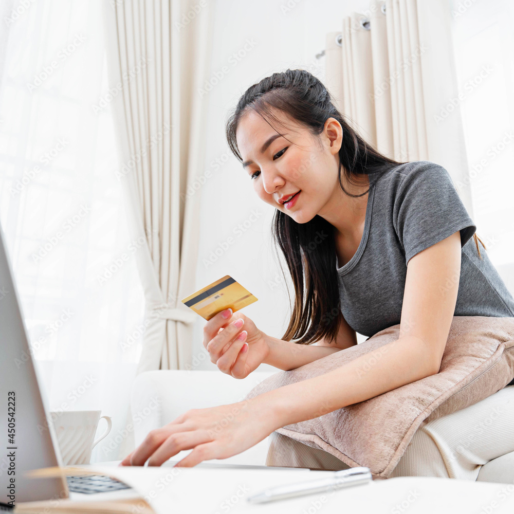Asian woman using credit card for online payment with laptop while sitting at the living room. online shopping Pay by credit card via electronic wallet. Asian woman using credit card for online payment with laptop while sitting at the living room. online shopping Pay by credit card via electronic wallet.