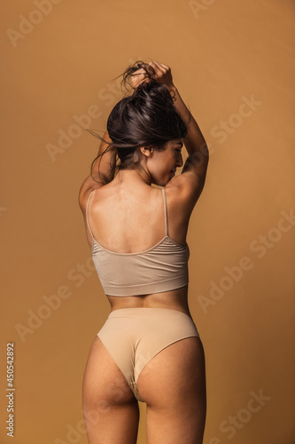 Back view of sportive body of young caucasian woman isolated on brown studio background. Natural beauty concept